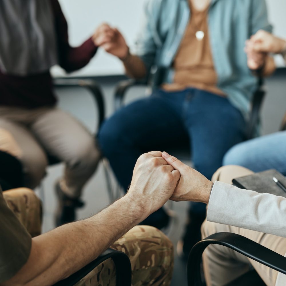 Close-up of group therapy attenders holding hands while sitting in a circle.